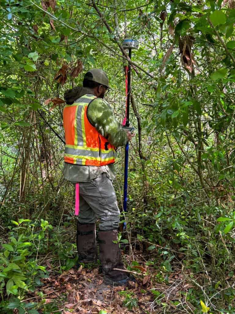 Surveyor using GPS equipment to collect boundary and site data in wooded property during land surveying work